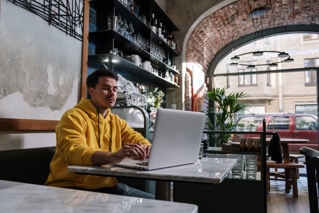 Person pausing at laptop in a café, mid-thought after an AI usage limit interrupts the workflow